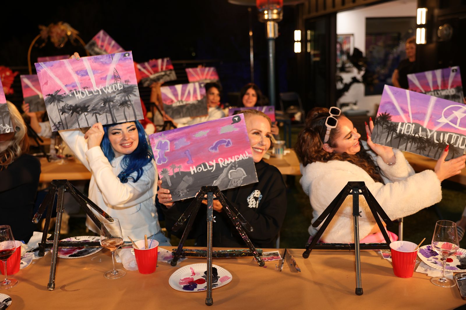 Cast members show off their finished Hollywood paintings at the Stripchat House sip and paint night