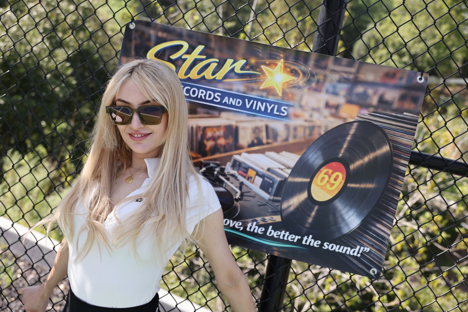 A cast member poses with her parody sponsor banner at the Stripchat House pickleball tournament
