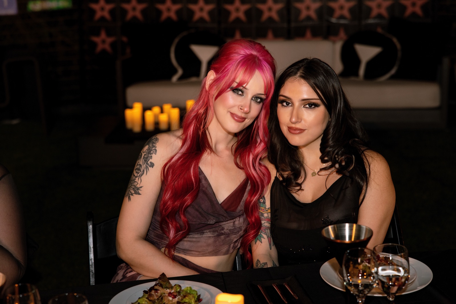 Two guests lean together at candlelit outdoor dinner table